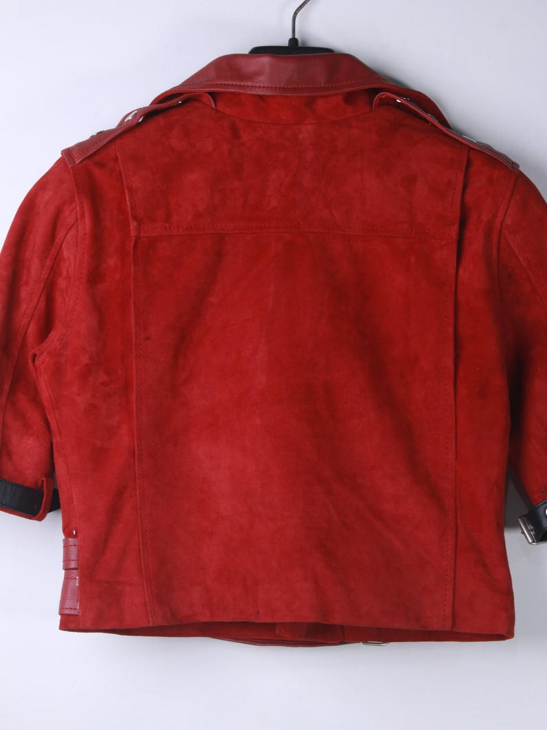 Puede incluir: Chaqueta de ante roja con cuello y detalles de cuero. La chaqueta presenta un estilo motero cl&aacute;sico con solapa de muesca, charreteras y detalle de cintur&oacute;n en la cintura. Las mangas tienen pu&ntilde;os negros.