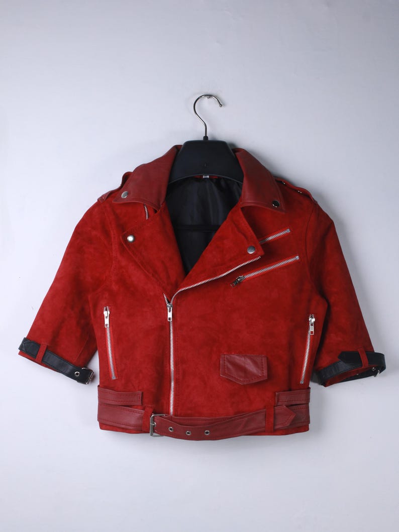 Puede incluir: Chaqueta de ante roja con cuello negro y mangas cortas. La chaqueta tiene cremalleras plateadas, cintur&oacute;n y pu&ntilde;os negros. La chaqueta est&aacute; colgada de una percha negra sobre un fondo blanco.