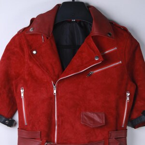 Puede incluir: Chaqueta roja de ante con estilo motero cl&aacute;sico. Cuenta con cuello con solapas, m&uacute;ltiples cremalleras plateadas, un peque&ntilde;o bolsillo y cintur&oacute;n en la cintura. La chaqueta est&aacute; colgada en una percha negra.