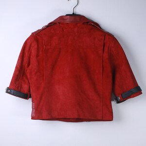 Puede incluir: Chaqueta de ante roja con mangas cortas, colgada de una percha. La chaqueta tiene detalles de cuero negro en el cuello y los pu&ntilde;os. La parte trasera de la chaqueta es visible, mostrando las costuras y el dise&ntilde;o.