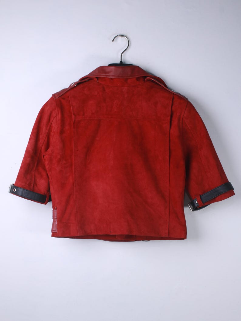Puede incluir: Chaqueta de ante roja con mangas cortas, colgada de una percha. La chaqueta tiene detalles de cuero negro en el cuello y los pu&ntilde;os. La parte trasera de la chaqueta es visible, mostrando las costuras y el dise&ntilde;o.
