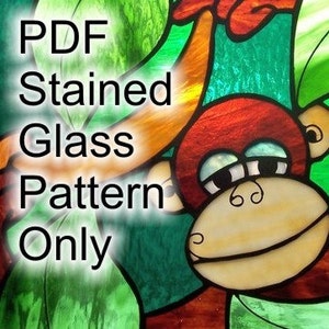 Può includere: Un modello di vetro colorato di una scimmia dei cartoni animati con pelliccia marrone, occhi gialli e bocca rossa. La scimmia è appesa a un ramo con foglie verdi. Il modello è etichettato "PDF Stained Glass Pattern Only".