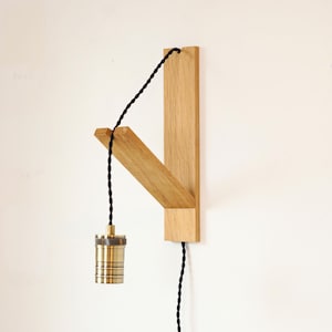 May include: A wooden wall-mounted light fitting with a black cord and a brass light bulb socket. The fitting has a simple, modern design and is perfect for adding a touch of industrial style to any room.