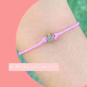 May include: A pink string bracelet with a silver crown charm. The bracelet has the text "A Princess Wish!" on the image.