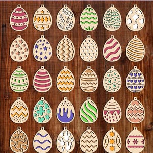 Może przedstawiać: Kolekcja drewnianych ozdób wielkanocnych w kształcie jajek z różnymi wzorami i kolorami, w tym gwiazdami, paskami i wzorami kwiatowymi. Ozdoby są prezentowane na tle ciemnego drewna.