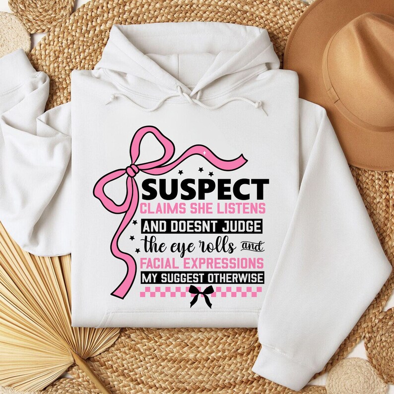 K&ouml;nnte beinhalten: Wei&szlig;er Hoodie mit einer rosa Schleife und schwarzem Text, der "SUSPECT CLAIMS SHE LISTENS AND DOESNT JUDGE the eye rolls and FACIAL EXPRESSIONS MY SUGGEST OTHERWISE" lautet.
