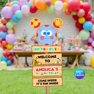 May include: A colorful birthday party sign featuring a cartoon character with a blue face and red polka dots. The sign reads "Oh Toodles", "Welcome to Anglica's 1st Birthday", and "Come Inside It's Fun Inside". Balloons and party decorations are in the background.