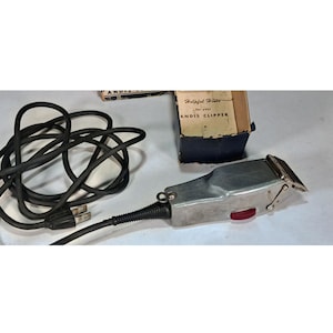 May include: A vintage silver-toned Andis clipper with a red power button and a black power cord. The clipper is accompanied by its original box, which reads "Helpful Hints for your ANDIS CLIPPER."