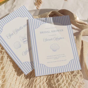 May include: Two invitation cards with blue and white striped borders. One card reads "Sea Shells and Wedding" with seashell and bell illustrations. The other card says "Bridal Shower" and includes event details.