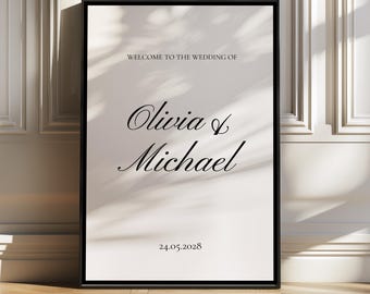 May include: A framed wedding sign with the text "WELCOME TO THE WEDDING OF Olivia & Michael" in elegant script. The date "24.05.2028" is displayed below. The sign is set against a neutral background with a black frame.