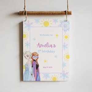 K&ouml;nnte beinhalten: Ein h&auml;ngendes Schild mit dem Text Welcome to Amelia's 5th birthday May 27 2029. Das Design zeigt Illustrationen von zwei Figuren mit blondem und kastanienbraunem Haar, umgeben von gelben Sonnensymbolen sowie blauen und violetten Schneeflocken.