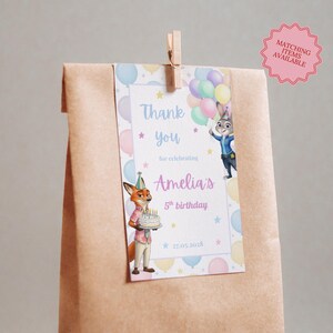 May include: A brown paper gift bag with a tag that says "Thank you for celebrating Amelia's 5th birthday." The tag features cartoon characters and balloons. A wooden clip holds the tag to the bag. A pink sticker says "Matching items available."