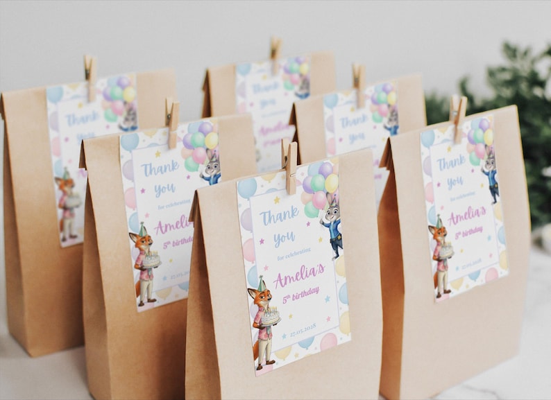 Pode incluir: Sacos de presente de papel castanho com etiquetas que dizem "Obrigado" e "5&ordm; anivers&aacute;rio da Amelia". As etiquetas apresentam personagens de desenhos animados e bal&otilde;es. Os sacos s&atilde;o fechados com molas de roupa de madeira.