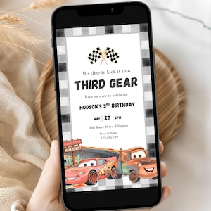 May include: A digital birthday invitation displayed on a smartphone screen featuring a black and white checkered border, two checkered flags, and the text It's time to kick it into THIRD GEAR for Hudson's 3rd birthday, with cartoon race cars.