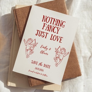 Könnte beinhalten: Eine weiße Hochzeitseinladung mit rotem Text und Illustrationen. Die Einladung trägt die Aufschrift "NOTHING FANCY JUST LOVE" und enthält die Namen "Emily & Oliver" sowie das Datum "24.05.2026". Der Satz "SAVE the DATE" ist ebenfalls vorhanden.