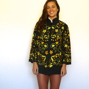 May include: A woman wearing a black jacket with yellow and orange floral embroidery. The jacket has a mandarin collar and long sleeves.