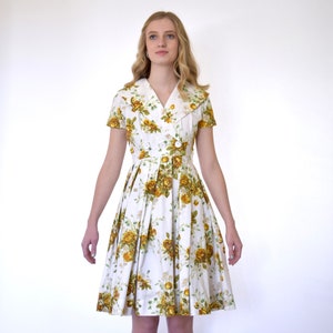 May include: A white dress with a yellow floral print and a large collar. The dress has short sleeves and a fitted bodice. The skirt is full and pleated.