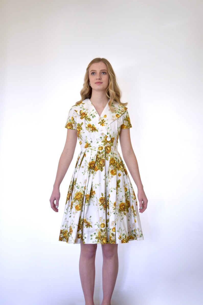 May include: A white dress with a yellow floral print and a large collar. The dress has short sleeves and a fitted bodice. The skirt is full and pleated.
