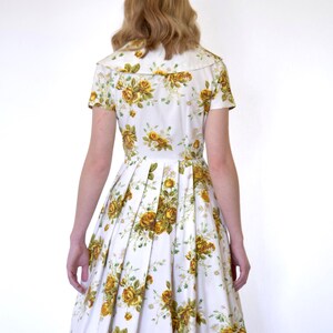 May include: A white dress with a yellow floral print and a white collar. The dress has a pleated skirt and short sleeves.