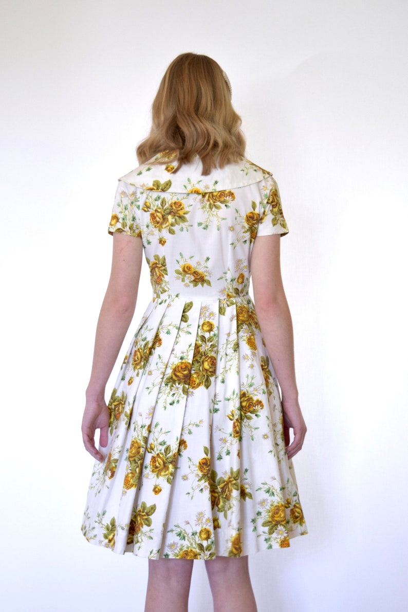 May include: A white dress with a yellow floral print and a white collar. The dress has a pleated skirt and short sleeves.