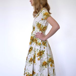 May include: A white dress with a yellow floral print. The dress has a collared neckline, short sleeves, and a pleated skirt.