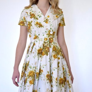 May include: A white dress with a yellow floral print and a large collar. The dress has a button closure and a pleated skirt.