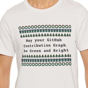 May include: A white crew neck t-shirt featuring a holiday-themed graphic print. The design includes rows of green wreaths, wrapped gifts, and Christmas trees, with the text: May your GitHub Contribution Graph be Green and Bright.