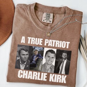 K&ouml;nnte beinhalten: Braunes Comfort Colors T-Shirt mit dem Text "A True Patriot Charlie Kirk" und vier Schwarz-Wei&szlig;-Bildern von Charlie Kirk. Eine silberne Halskette mit Anh&auml;nger befindet sich auf dem Shirt.