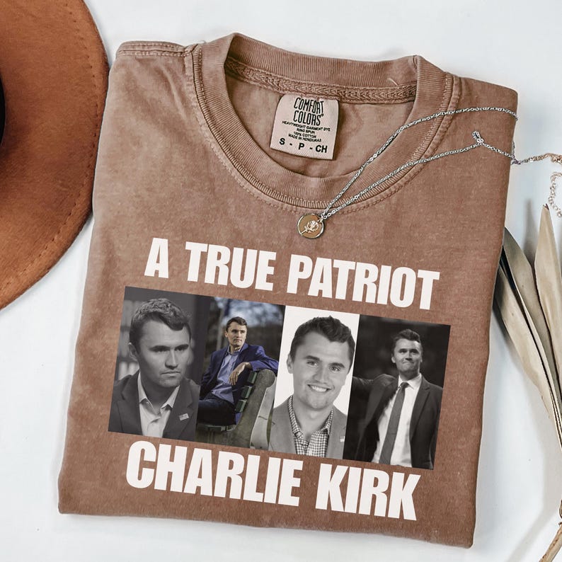 K&ouml;nnte beinhalten: Braunes Comfort Colors T-Shirt mit dem Text "A True Patriot Charlie Kirk" und vier Schwarz-Wei&szlig;-Bildern von Charlie Kirk. Eine silberne Halskette mit Anh&auml;nger befindet sich auf dem Shirt.