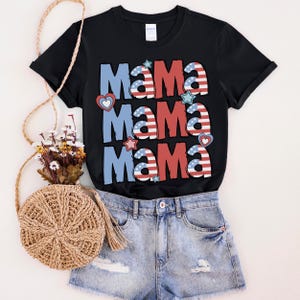 May include: Black t-shirt with the word "Mama" in red, white, and blue, with stars and hearts. The shirt is paired with denim shorts and a woven bag with a floral arrangement.