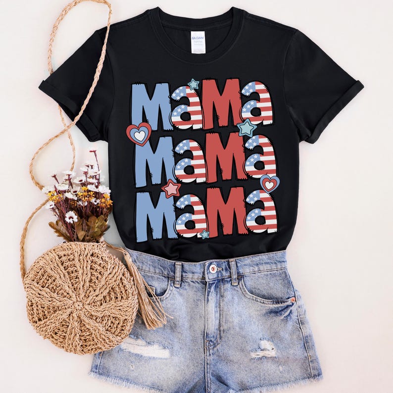 May include: Black t-shirt with the word "Mama" in red, white, and blue, with stars and hearts. The shirt is paired with denim shorts and a woven bag with a floral arrangement.