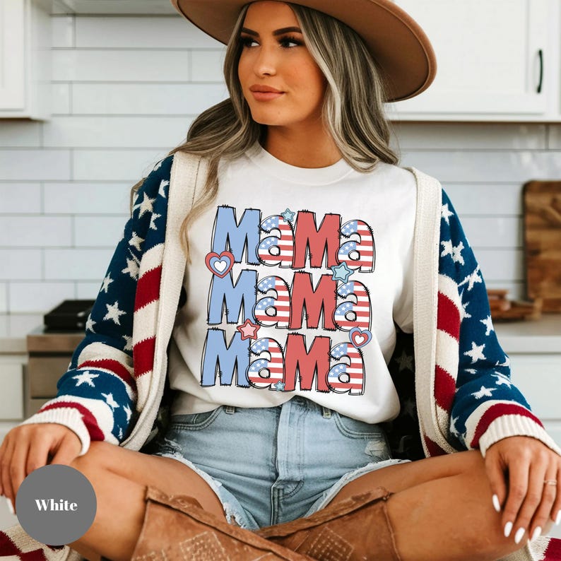 May include: White t-shirt with the word "Mama" repeated three times in red, white, and blue, with heart and star accents. The shirt is paired with denim shorts and a cardigan with a star-spangled design.