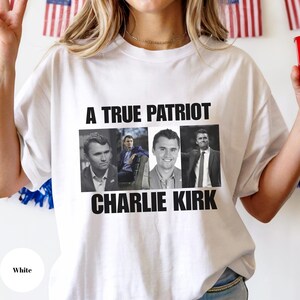 K&ouml;nnte beinhalten: Wei&szlig;es T-Shirt mit dem Text "A TRUE PATRIOT CHARLIE KIRK" in schwarzen Blockbuchstaben. Das Shirt zeigt vier Graustufenbilder eines Mannes. Das Wort "White" befindet sich in einem wei&szlig;en Kreis unten links.