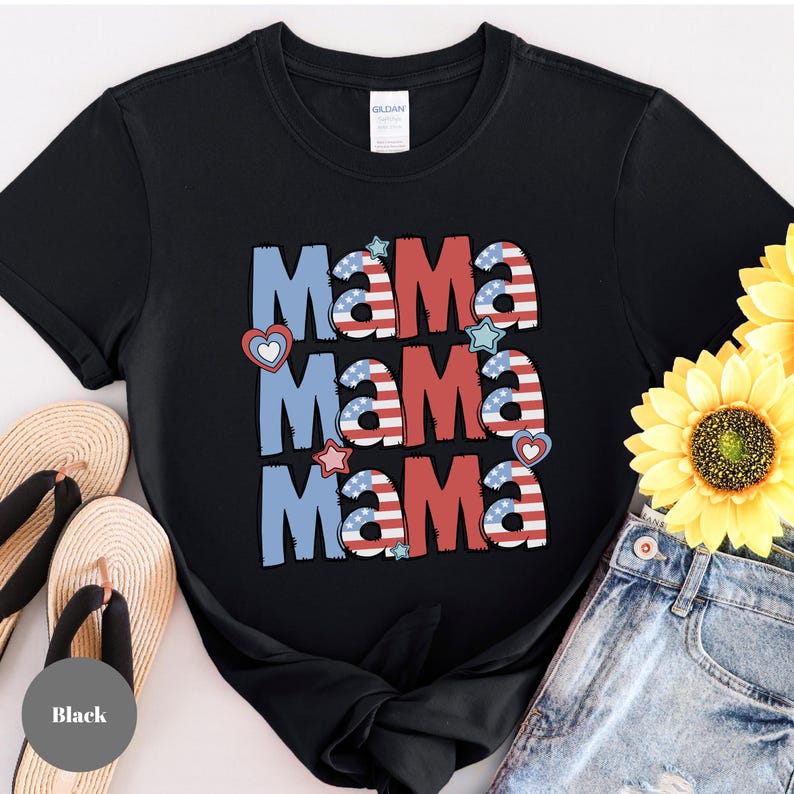 May include: Black t-shirt with the word "Mama" in red, white, and blue, with heart and star accents. The letters are designed to resemble the American flag. The shirt is paired with denim shorts and sandals.