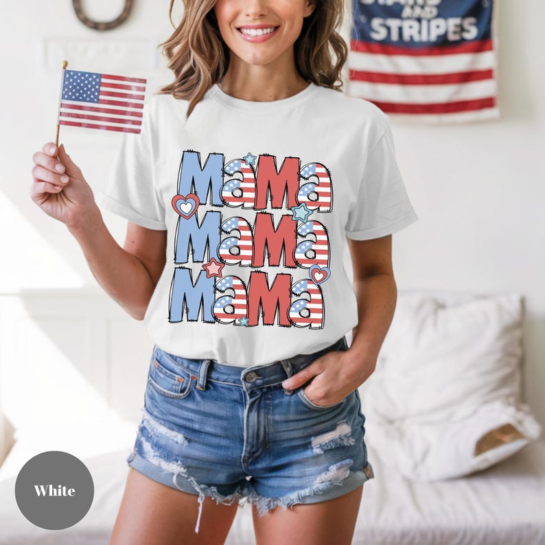 May include: White t-shirt with the word "Mama" repeated three times in red, white, and blue, with heart and star accents. The design has an American flag theme. The shirt is short-sleeved.