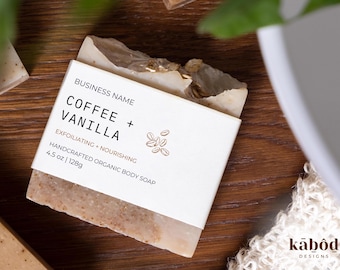 May include: A white bar of soap with a brown label that reads "BUSINESS NAME COFFEE + VANILLA EXFOLIATING NOURISHING HANDCRAFTED ORGANIC BODY SOAP 4.5 oz | 128g".