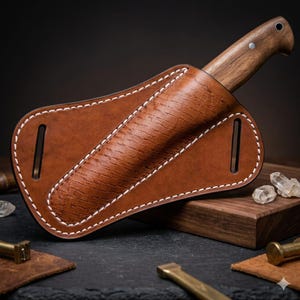 May include: A handcrafted knife with a wooden handle is partially sheathed in a brown leather holster. The holster features white stitching and a textured design. The knife and holster are displayed on a wooden block.