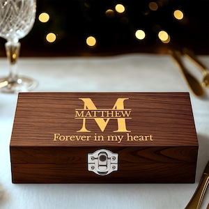 May include: A wooden box with a hinged lid and a silver clasp. The box is engraved with the name "Matthew" above the words "Forever in my heart" in a gold color. The box is made of a dark brown wood.