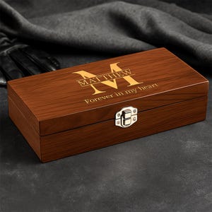 May include: A rectangular wooden box with a hinged lid and a silver clasp. The box is engraved with the name "MATTHEW" above the phrase "Forever in my heart" in a gold color. The wood grain is visible.