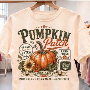 May include: A cream-colored t-shirt featuring a graphic print with a large orange pumpkin, sunflowers, and text that reads Pumpkin Patch, Fresh from the Patch, Farm Fresh, Locally Grown, Autumn Market, Pumpkins, Corn Maze, and Apple Cider.