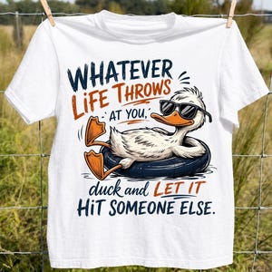 White t-shirt hanging on an outdoor clothesline featuring a funny duck wearing sunglasses in a black float with the quote "Whatever Life Throws At You, Duck and Let It Hit Someone Else," perfect for humorous fall and casual apparel.