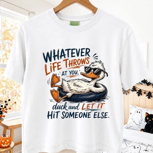 White hanging t-shirt mockup in a cozy fall-themed room featuring a cool duck wearing sunglasses on a float with the humorous quote "Whatever Life Throws At You, Duck and Let It Hit Someone Else.