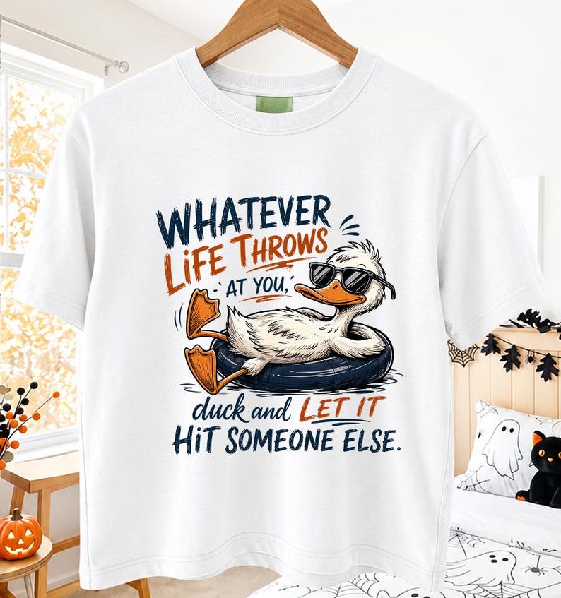 White hanging t-shirt mockup in a cozy fall-themed room featuring a cool duck wearing sunglasses on a float with the humorous quote "Whatever Life Throws At You, Duck and Let It Hit Someone Else.