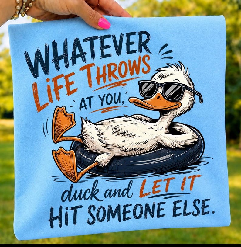 Folded light blue t-shirt mockup showcasing a funny duck wearing black sunglasses relaxing in an inner tube with the quote "Whatever Life Throws At You, Duck and Let It Hit Someone Else," in bold retro typography