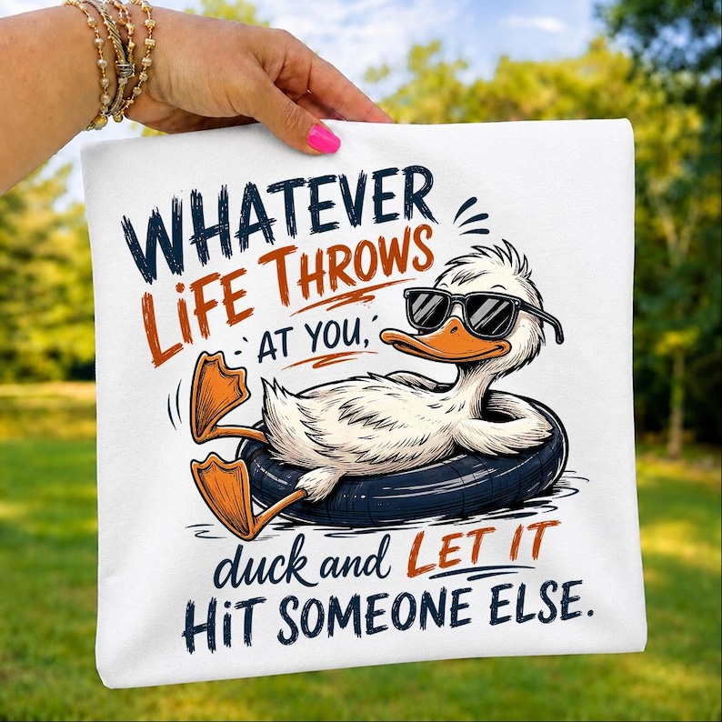 Folded white t-shirt mockup displaying a sarcastic duck lounging in an inflatable tube with sunglasses and the funny quote "Whatever Life Throws At You, Duck and Let It Hit Someone Else," ideal for humorous graphic tee lovers