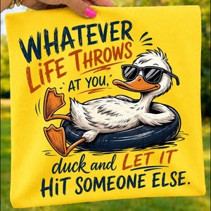Folded yellow t-shirt mockup featuring a cool cartoon duck floating in a black tube with sunglasses and the humorous quote "Whatever Life Throws At You, Duck and Let It Hit Someone Else," perfect for funny summer and casual gifts.