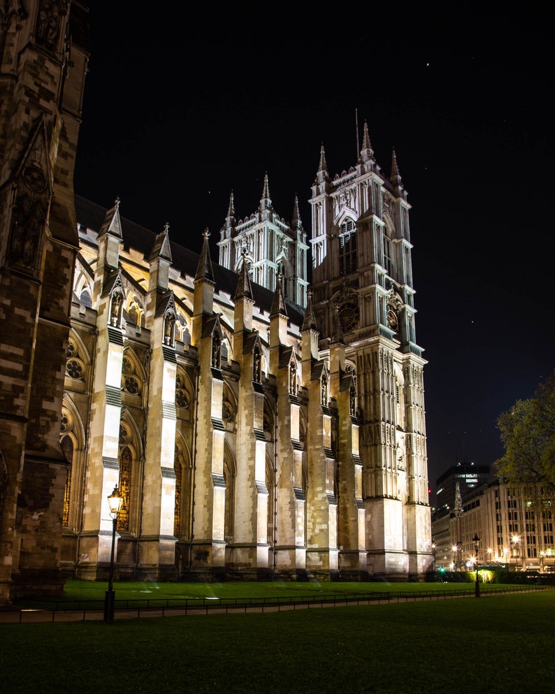 May include: A night view of Westminster Abbey in London, England. The abbey is illuminated with spotlights, highlighting its intricate architecture and tall towers. The building is made of stone and has a light brown color.