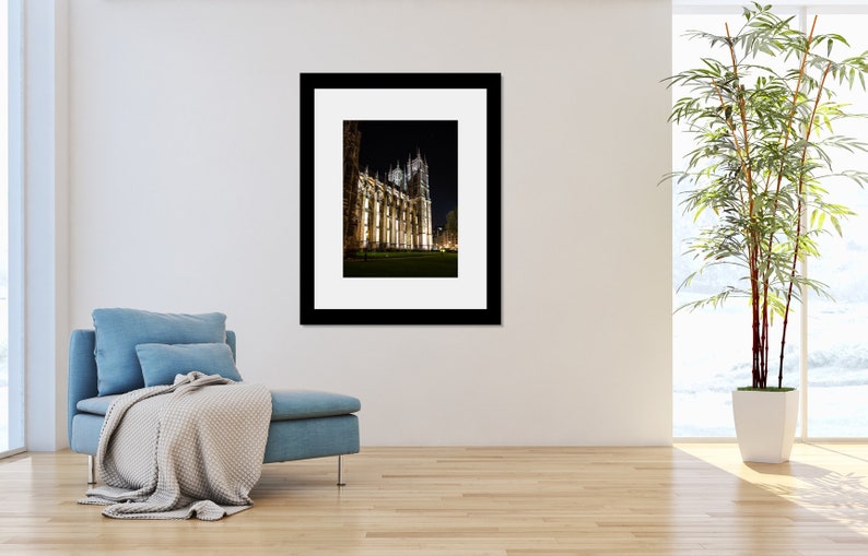 May include: A black and white photograph of a large, illuminated building at night. The building has a tall, pointed spire and many windows. The building is surrounded by a dark, grassy area.