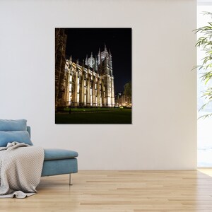 May include: A night view of a large, illuminated stone building with a tall spire. The building is surrounded by a grassy lawn and trees.