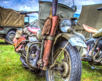 May include: A vintage motorcycle with a brown leather saddle and a windshield. The motorcycle has a brown leather saddlebag and a brown leather holster on the side. The motorcycle has a large front tire and a smaller rear tire. The motorcycle is parked on a grassy field.